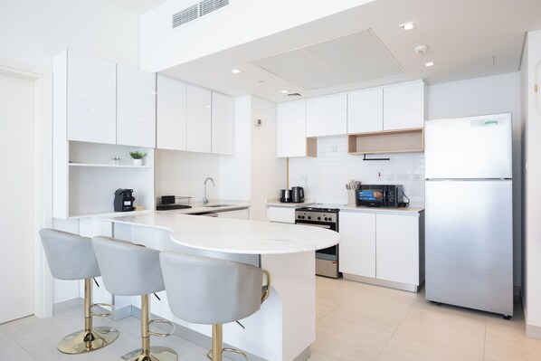 A modern kitchen with white cabinetry, a central island with bar stools, stainless steel appliances, and a tiled backsplash.