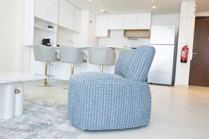 A modern living room with a blue patterned armchair, a white coffee table, and a grey sofa.