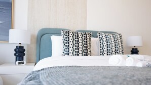 A neatly made bed with a patterned pillow, a bedside table with a lamp, and a wall clock. - Bloomfields 2BR in The Bridges - Reem (Abu Dhabi)