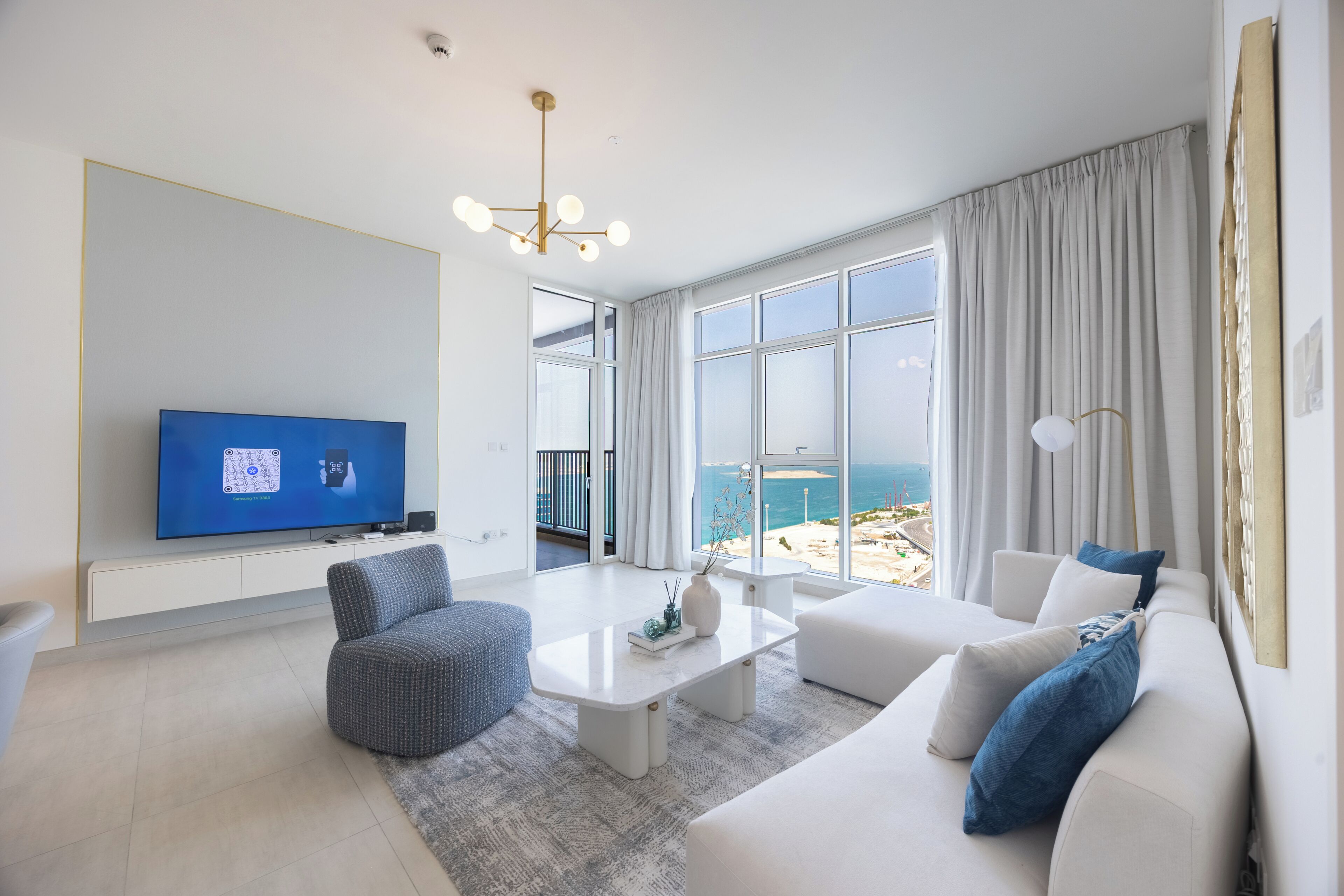 A modern living room with a television, seating, and a view of the sea.
