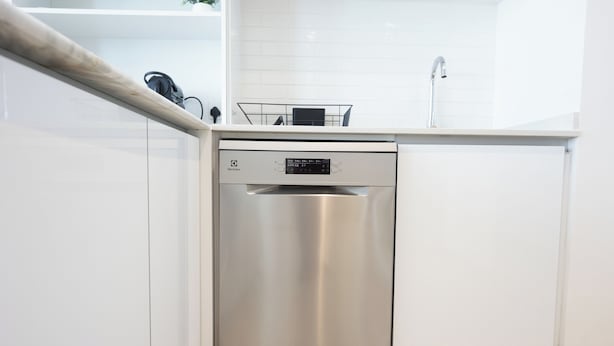 A modern kitchen with a stainless steel dishwasher, white cabinets, and a white countertop. - Bloomfields 2BR in The Bridges - Reem (Abu Dhabi)