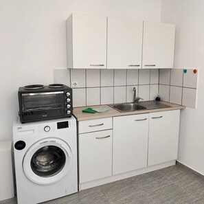 Eine kleine Küche mit integriertem Geschirrspüler, einem kleinen Backofen und einem Spülbecken.