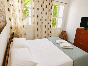 A hotel room with a bed, a television, a dresser, and a window with curtains. - Kalymnos Island Pearl - Seaside Getaway (Kalymnos)