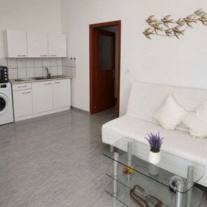A modern kitchen with white cabinets and a built-in oven, a glass coffee table with decorative items, and a white sofa with cushions. - Kalymnos Island Pearl - Seaside Getaway (Kalymnos)