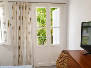 Et værelse med en seng, et fjernsyn på et træstel og en hvid dør med glasruder, samt et gardin med et mønster.