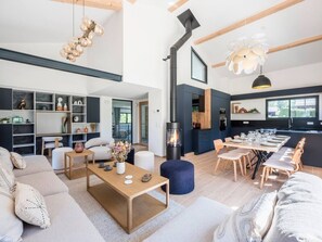 A modern living room with a fireplace, dining area, and built-in shelving. - Chalet 4BR – Nordic bath – parking and garage (Chamonix)
