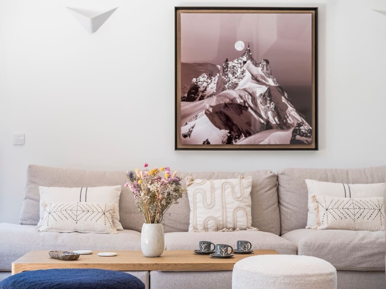 A living room with a sofa, a coffee table with a vase of flowers, and a framed picture on the wall.