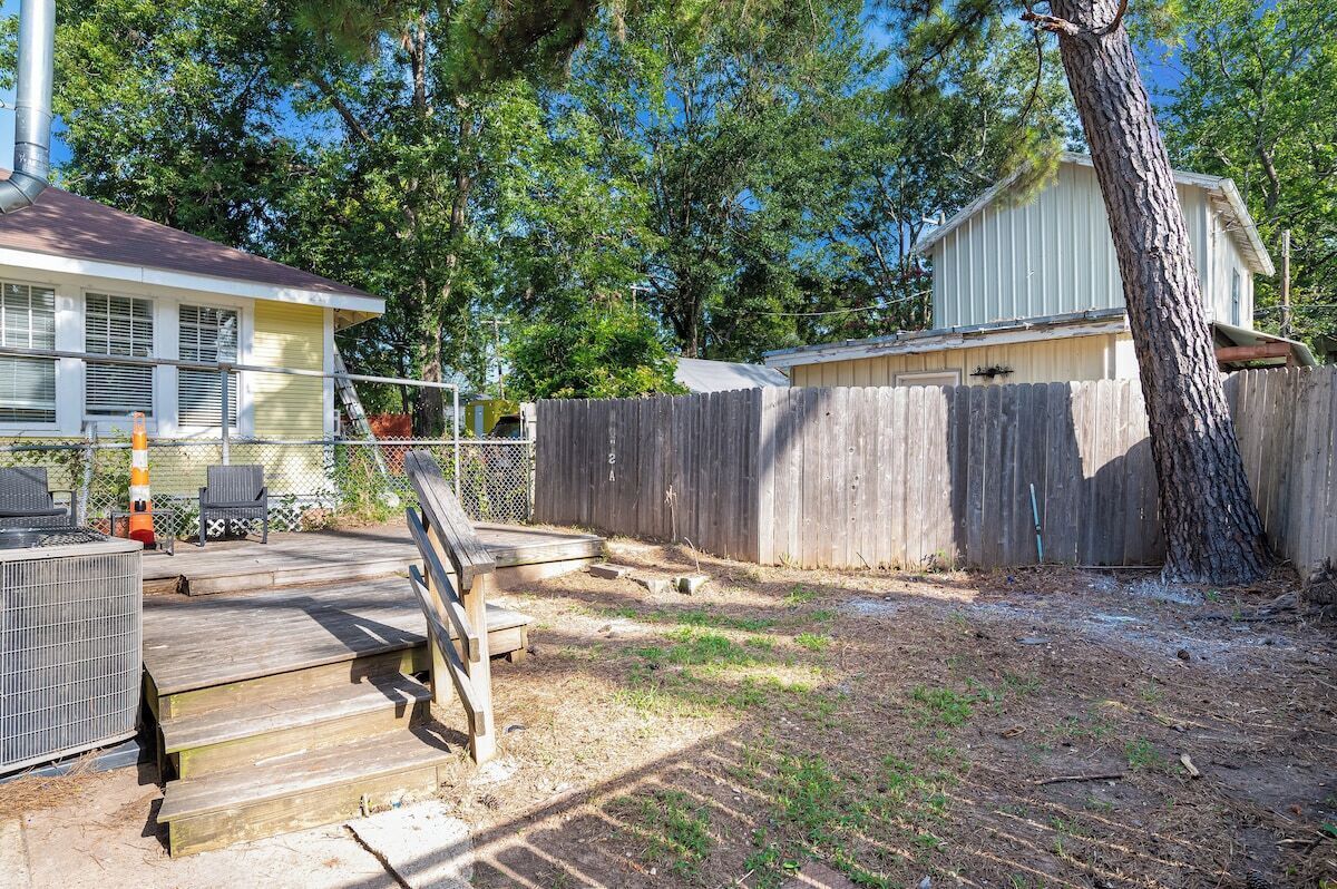 Une cour arrière clôturée avec une terrasse en bois, un arbre et un bâtiment en arrière-plan.