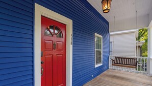 A blue house with a red door, a white garage door, and a porch with a bench. - 3 bedroom, 1.5 bathroom single family home in the Historic Highland Neighborhood (Shreveport)