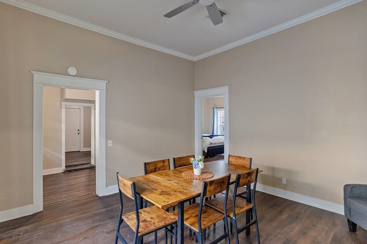 A dining area with a wooden table and chairs, a ceiling fan, and a view into another room.