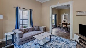 A living room with a sofa, coffee table, and a TV. There's a dining area with chairs and a table. The room has beige walls and a ceiling fan. - 3 bedroom, 1.5 bathroom single family home in the Historic Highland Neighborhood (Shreveport)