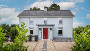 A two-story house with a red door, a small porch, and a gravel driveway. - Bealtaine (Síor Collection) (Carrick-On-Shannon)