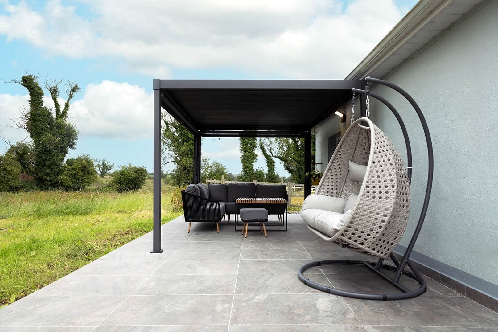 Un patio exterior con una zona de estar cubierta, una silla colgante y una parrilla.