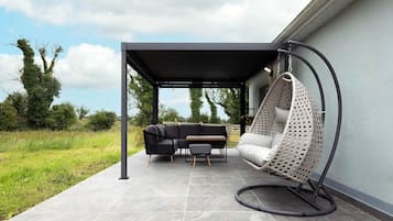 Un patio exterior con una zona de estar cubierta, una silla colgante y una parrilla.