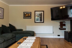 A living room with a sofa, a coffee table with coasters, a TV, and framed pictures on the wall.