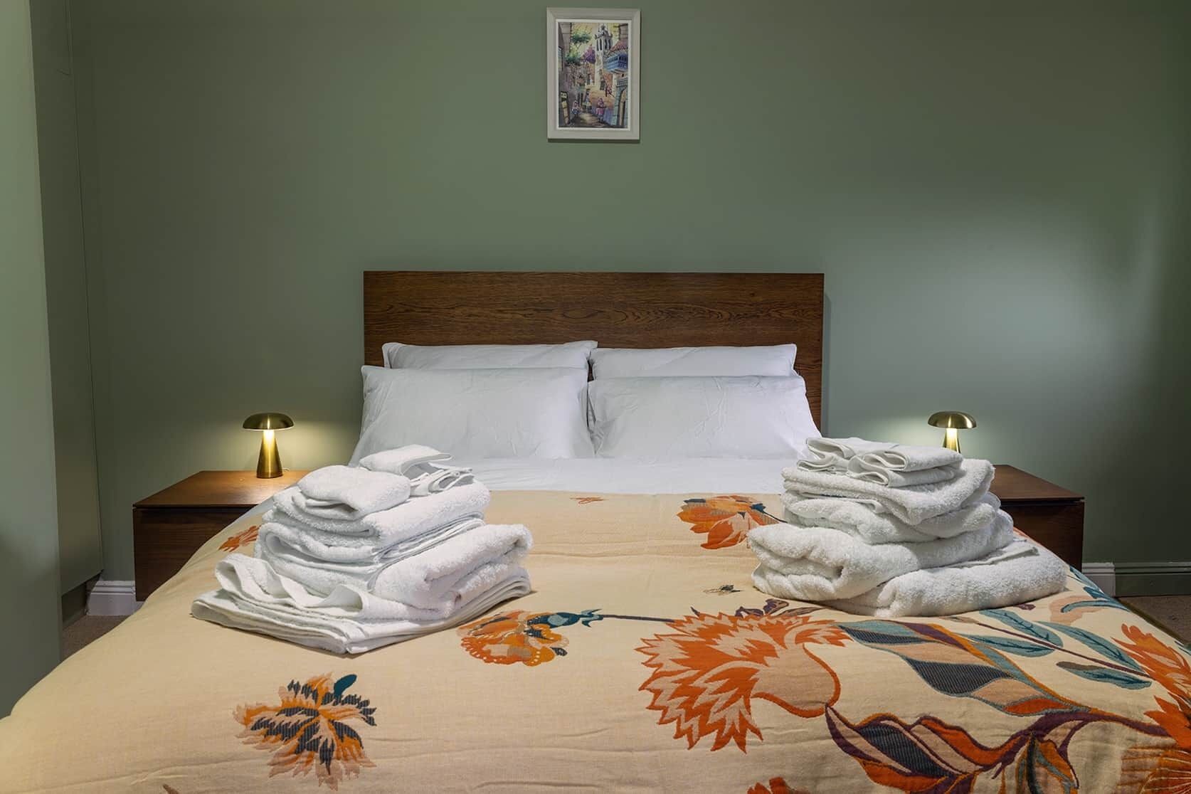 Une chambre d’hôtel avec un lit, deux tables de chevet, une lampe sur chacune, et une couvre-lit à motifs floraux.