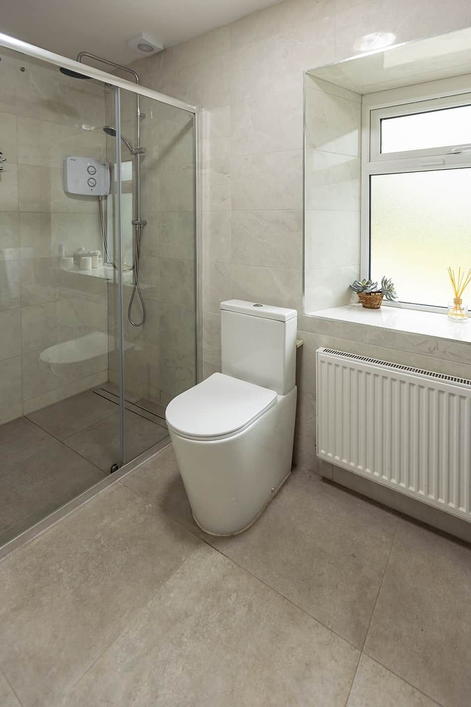A modern bathroom with a glass-enclosed shower, a white toilet, and a window with a view.