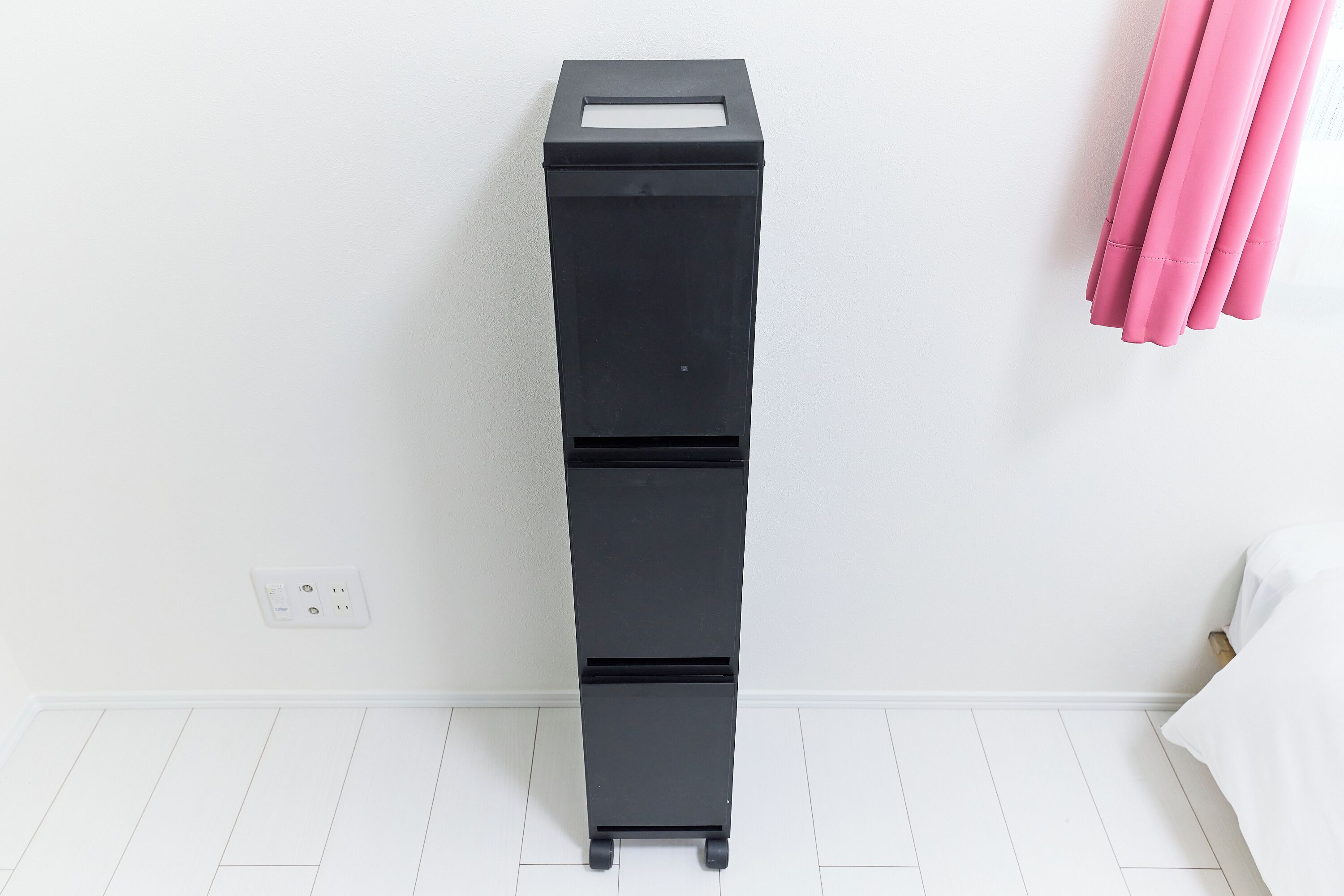 Un contenedor de almacenamiento negro con ruedas en una habitación con paredes y piso blancos.