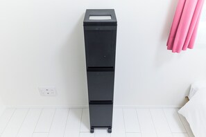 Un contenedor de almacenamiento negro con ruedas en una habitación con paredes y piso blancos.
