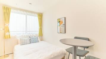 Habitación de hotel con cama, una mesa redonda y dos sillas, un cuadro en la pared y una lámpara de pie.