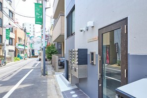 Vista de la calle con un edificio que tiene entrada protegida, cámara de seguridad y señalización de estacionamiento.