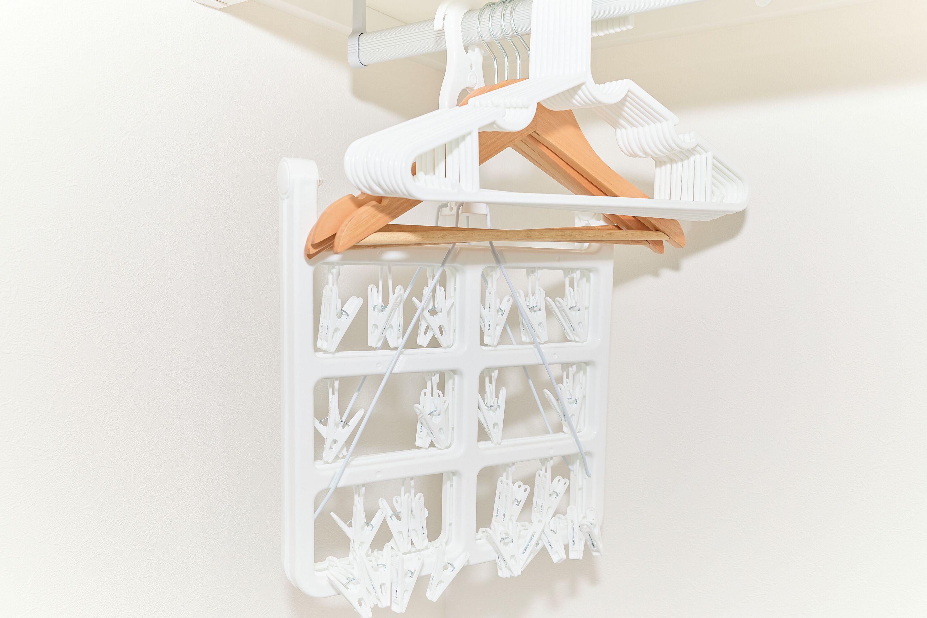 Een wit wandrek met houten kleerhangers en witte plastic knijpers.