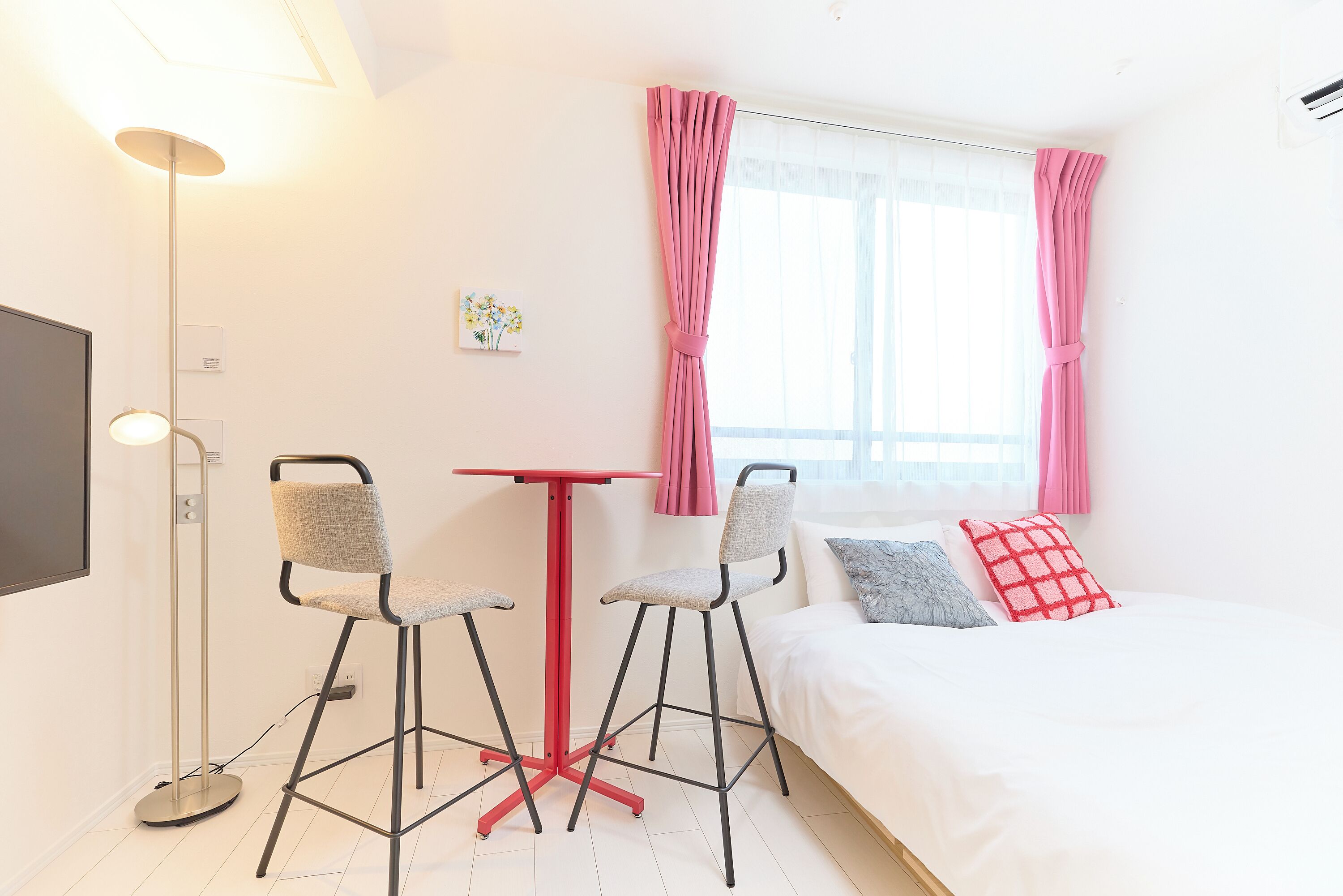 A hotel room with a bed, two chairs, a small table, a floor lamp, and a window with curtains.