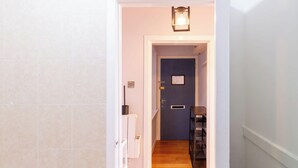 Um corredor com uma porta que dá para um quarto, uma luminária acima da porta e uma pequena mesa com uma cadeira.
