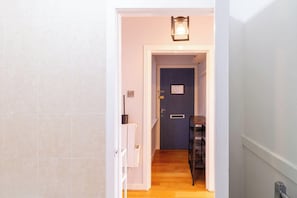 Ein Flur mit einer Tür zu einem Zimmer, einer Lampe über der Tür und einem kleinen Tisch mit Stuhl.