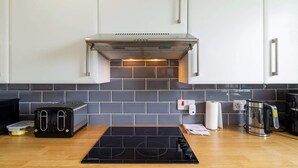 Uma cozinha moderna com um fogão por indução preto, uma torradeira, uma chaleira e uma cafeteira.