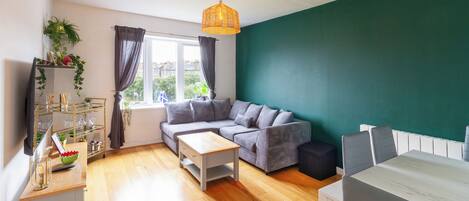 A modern living room with a sofa, a coffee table, a TV, and a dining area with a table and chairs.