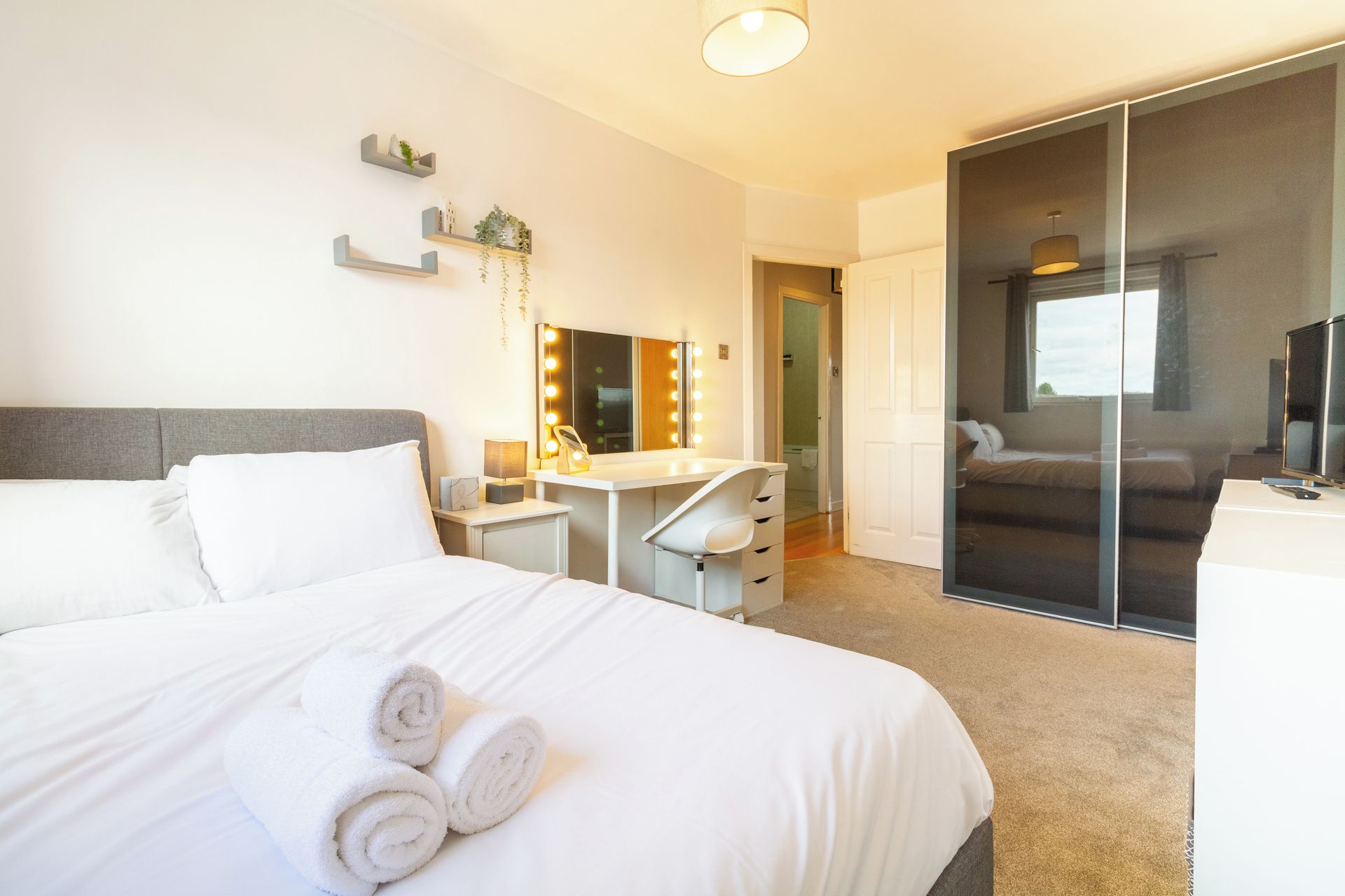 A hotel room with a bed, a desk with a mirror, and a sliding door leading to a bathroom.