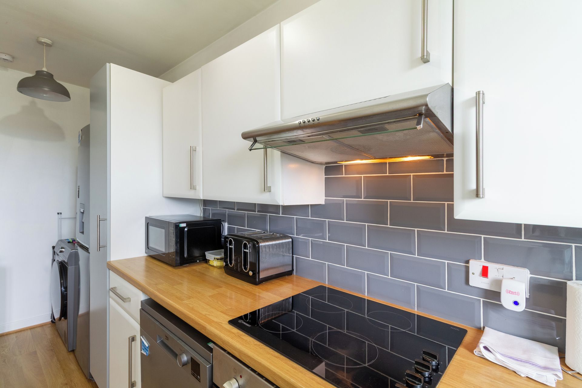 A modern kitchen with white cabinets, a black induction cooktop, a microwave, and a toaster.