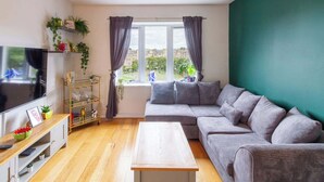 Uma sala de estar com televisão, sofá, mesa de centro e uma janela com cortinas.