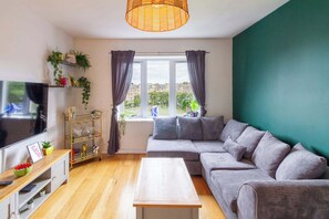 Ein Wohnzimmer mit Fernseher, Sofa, Couchtisch und einem Fenster mit Vorhängen.