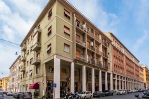 A multi-story building with balconies, a blue sign, and parked cars. - GuestHost - Bright Apartment in Piombino (Piombino)