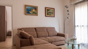 Sala de estar com um sofá marrom, duas pinturas na parede, um abajur e uma mesa de centro de vidro.