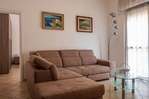 Ein Wohnzimmer mit einem braunen Sofa, zwei Bildern an der Wand, einer Stehlampe und einem Glastisch.