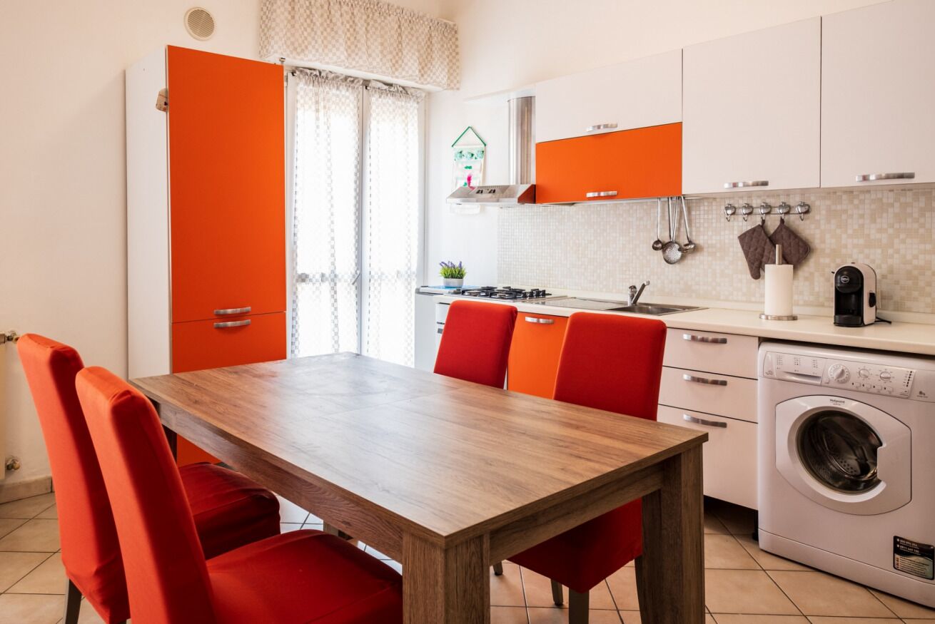 Une cuisine moderne avec une table en bois et des chaises rouges, un lave-linge et une fenêtre avec des rideaux.