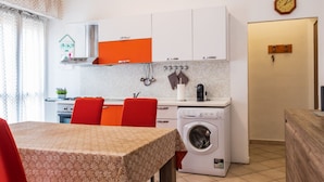 A compact kitchen with a washing machine, a dining table with chairs, and a clock on the wall.