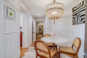 A dining area with a round table, wicker chairs, a chandelier, and a framed abstract painting. - Midnight Garden A - Refined Stay Neighboring the Mercer Williams House on Monterey Square (Savannah)
