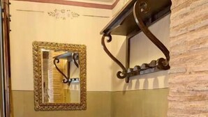 Ein schmaler Flur mit einem Holzschrank, einem Spiegel mit dekorativem Rahmen und einem Wandregal.