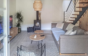 Ein modernes Wohnzimmer mit einer Couch, zwei kleinen Tischen, einer Zierlampe, einer Treppe und einem Blumentopf.