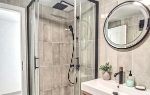 A modern bathroom with a glass-enclosed shower, a round mirror, and a sink with toiletries. - Lovely home in Kucice with house a panoramic view (Kucice)