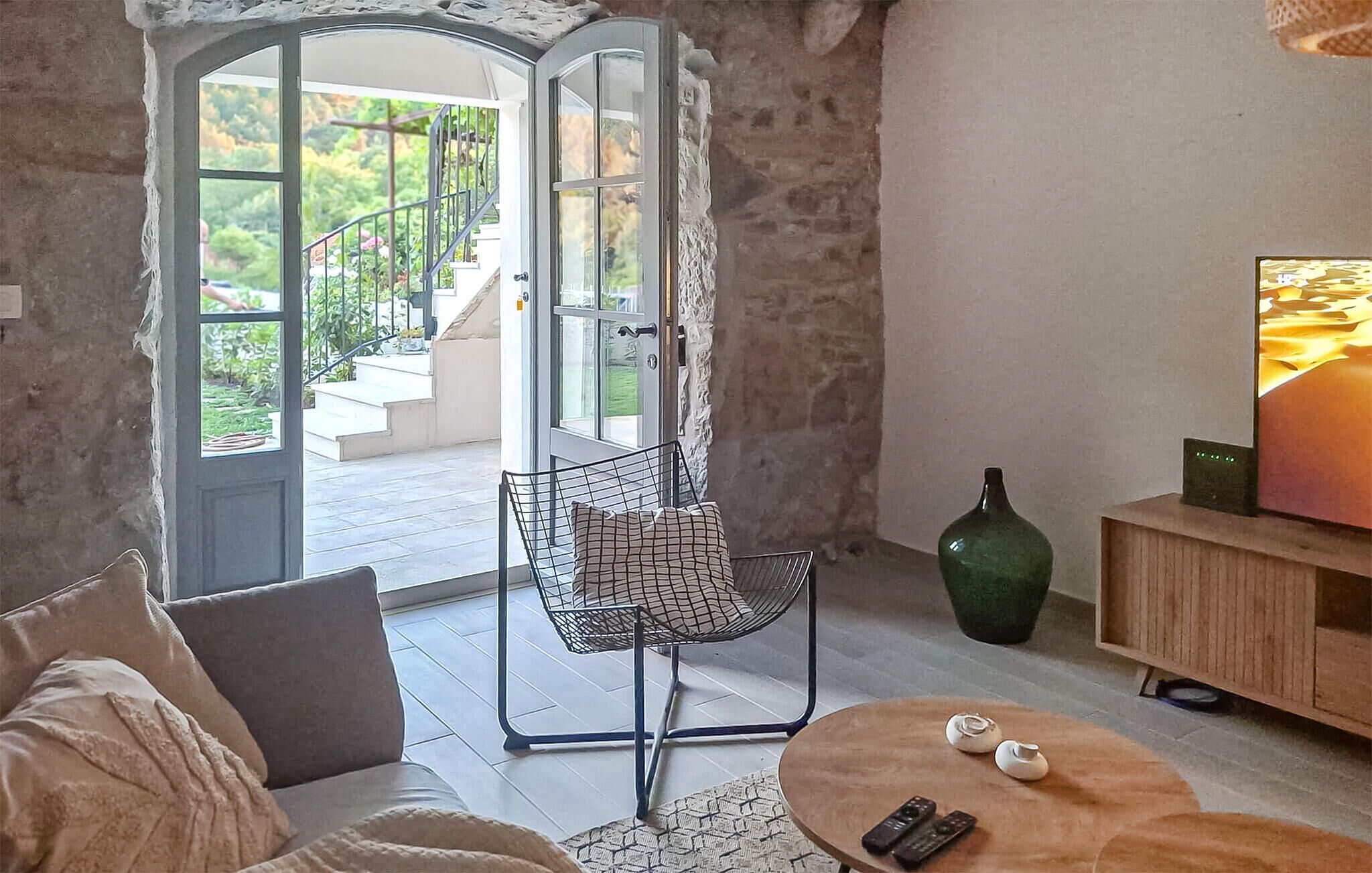 A living room with a sofa, a coffee table, a chair, a TV, and a view of a staircase leading to a balcony.