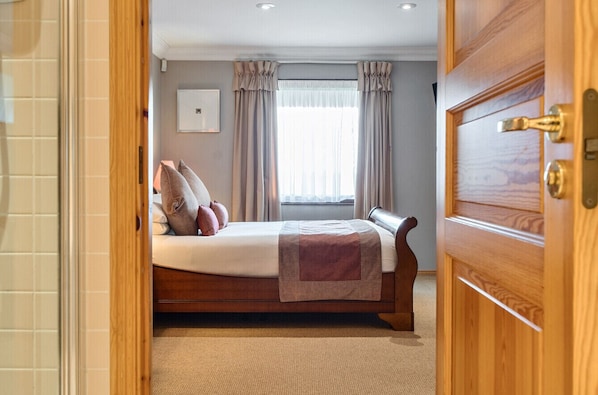 A bedroom with a bed, curtains, a window, and a wooden door.