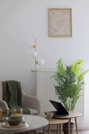 A minimalist living space with a radiator, a green plant, a laptop on a small table, and a framed abstract artwork on the wall. - Stylish Studios with Balconies | Close to the Underground | City Centre (Warszawa)