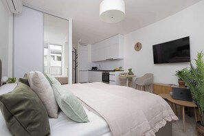A modern bedroom with a bed, a desk, a chair, a TV, and a kitchen in the background. - Stylish Studios with Balconies | Close to the Underground | City Centre (Warszawa)