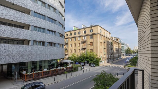 A street view with modern buildings, a café with outdoor seating, and parked cars. - Stylish Studios with Balconies | Close to the Underground | City Centre (Warszawa)