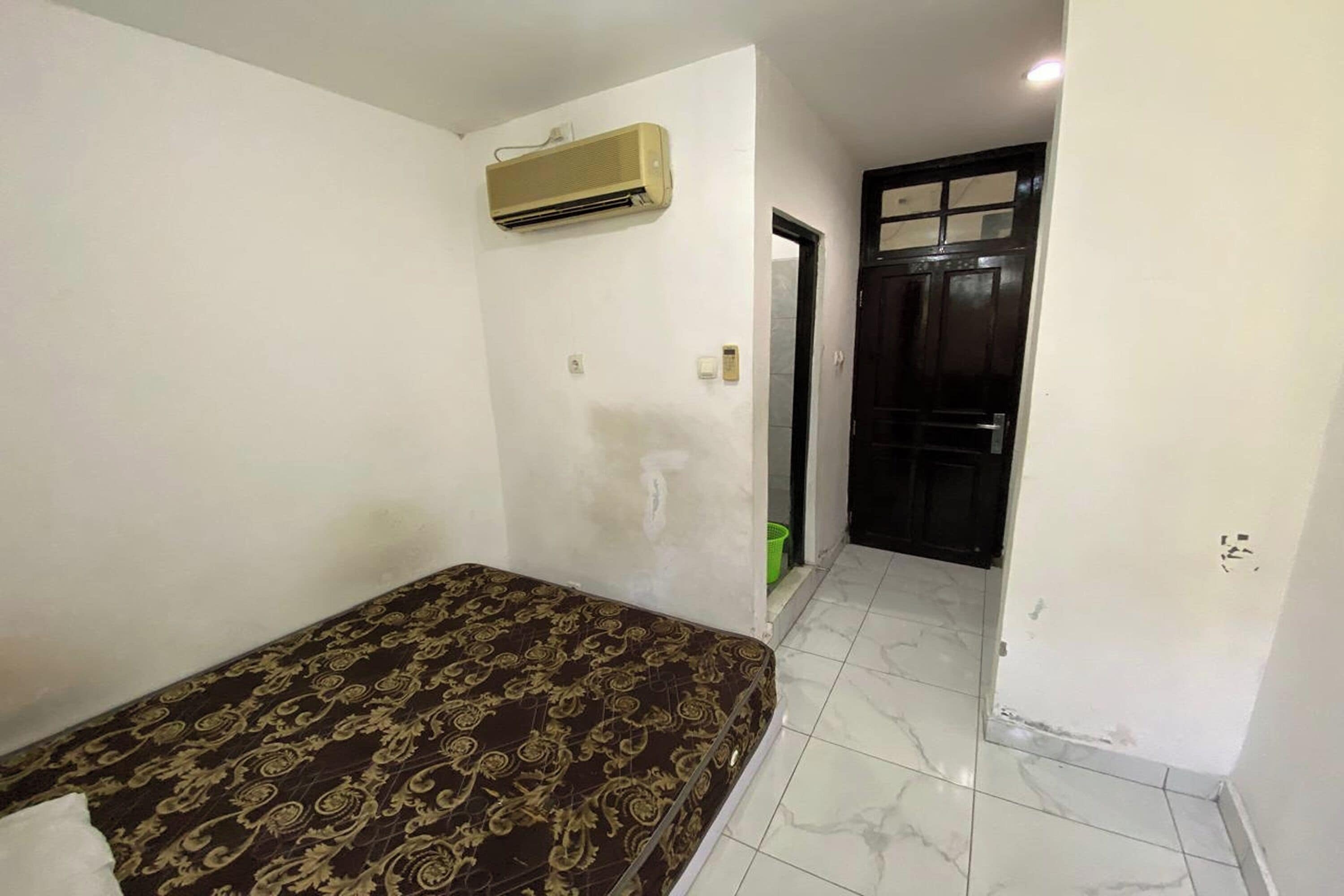 Una habitación con cama, aire acondicionado, una puerta y piso de baldosas.